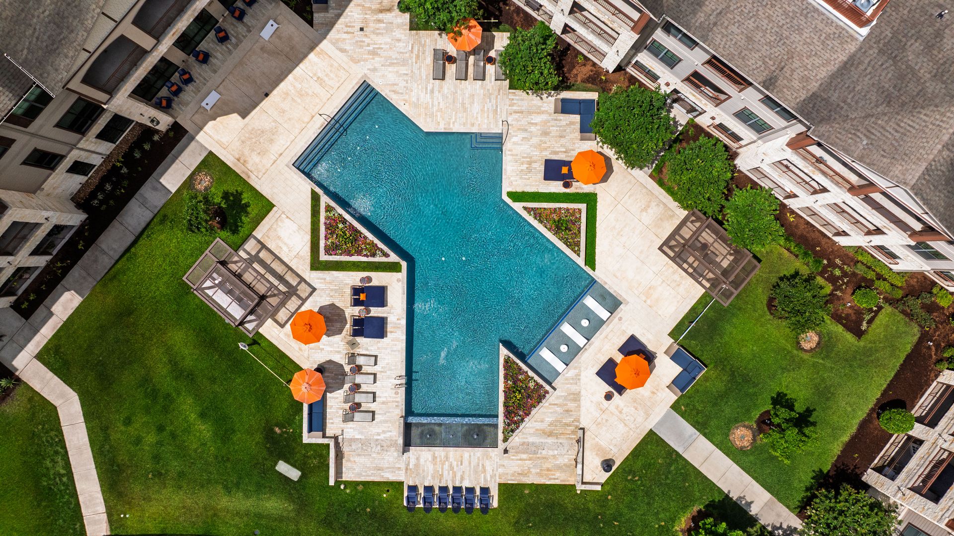 Aerial view of a turquoise swimming pool with lounge chairs and umbrellas in a landscaped resort courtyard at Olympus Auburn Lakes in Spring, TX.