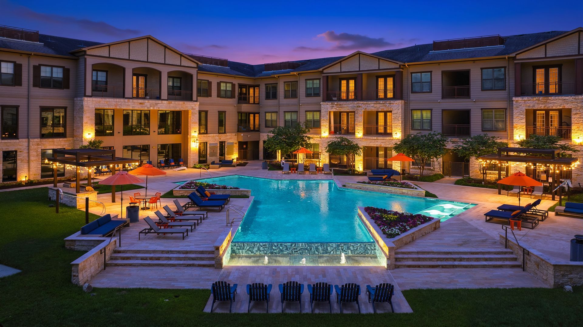 Luxury apartment courtyard with lit pool, hot tubs, and lounge chairs at dusk at Olympus Auburn Lakes in Spring, TX.
