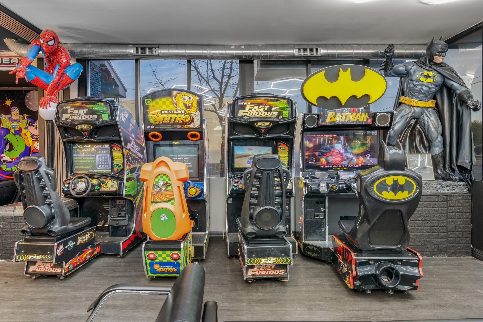 Batman-themed room with arcade machines, Batman statues, and superhero toys on display.