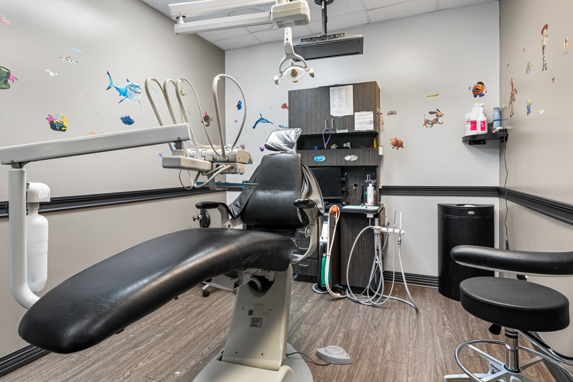 Dentist office with reclining exam chair, overhead light, cabinets, and dental tools on a clean white room.