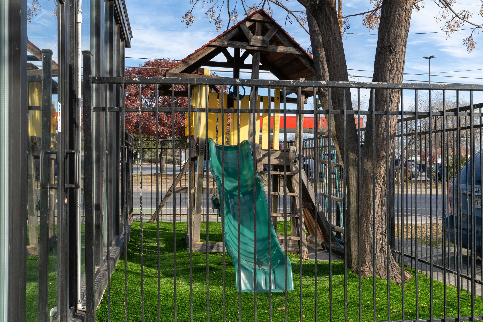 Backyard playground with a green slide inside a fenced yard under trees