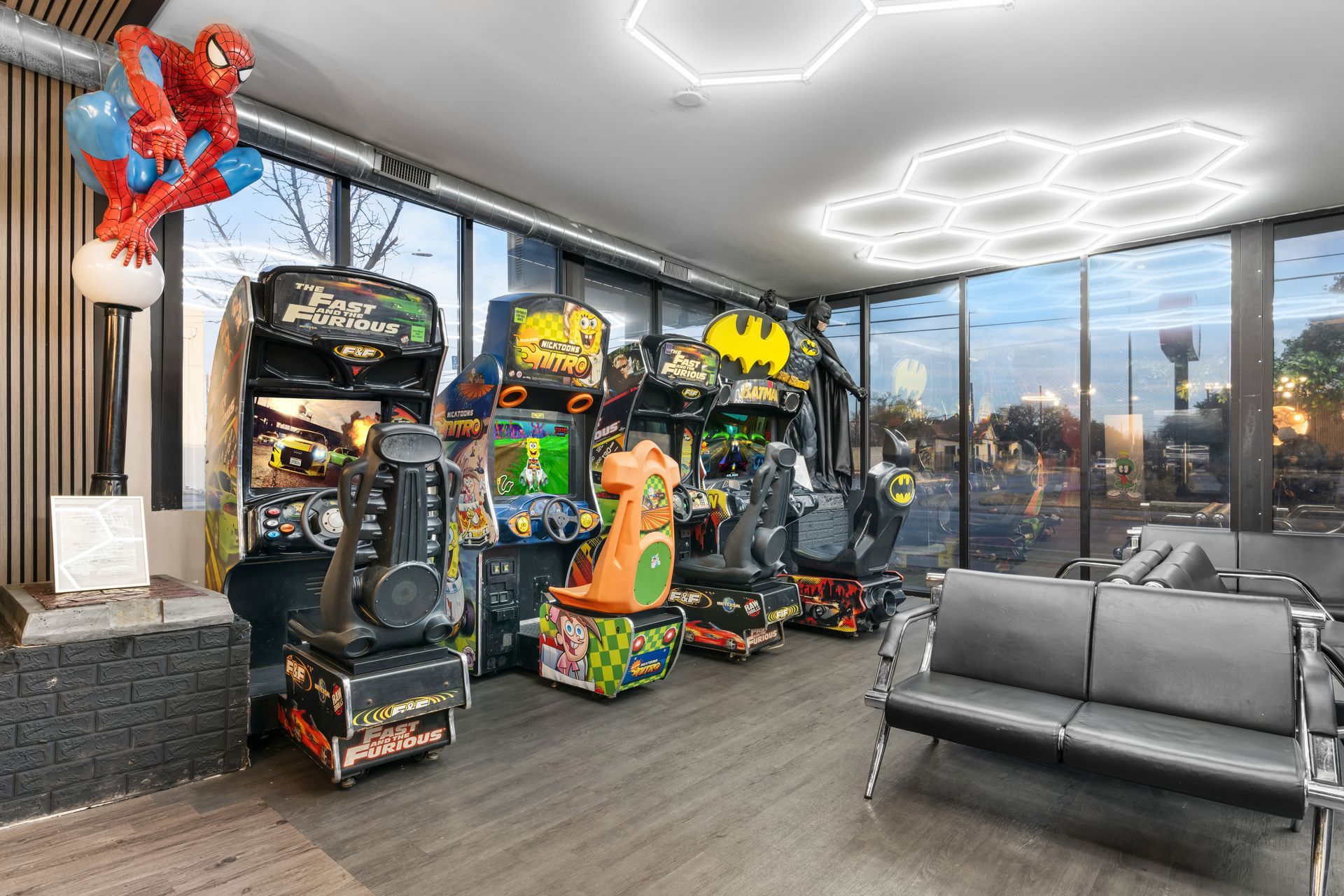 Arcade room with several game machines, Spider-Man wall art, and a gray sectional by large windows