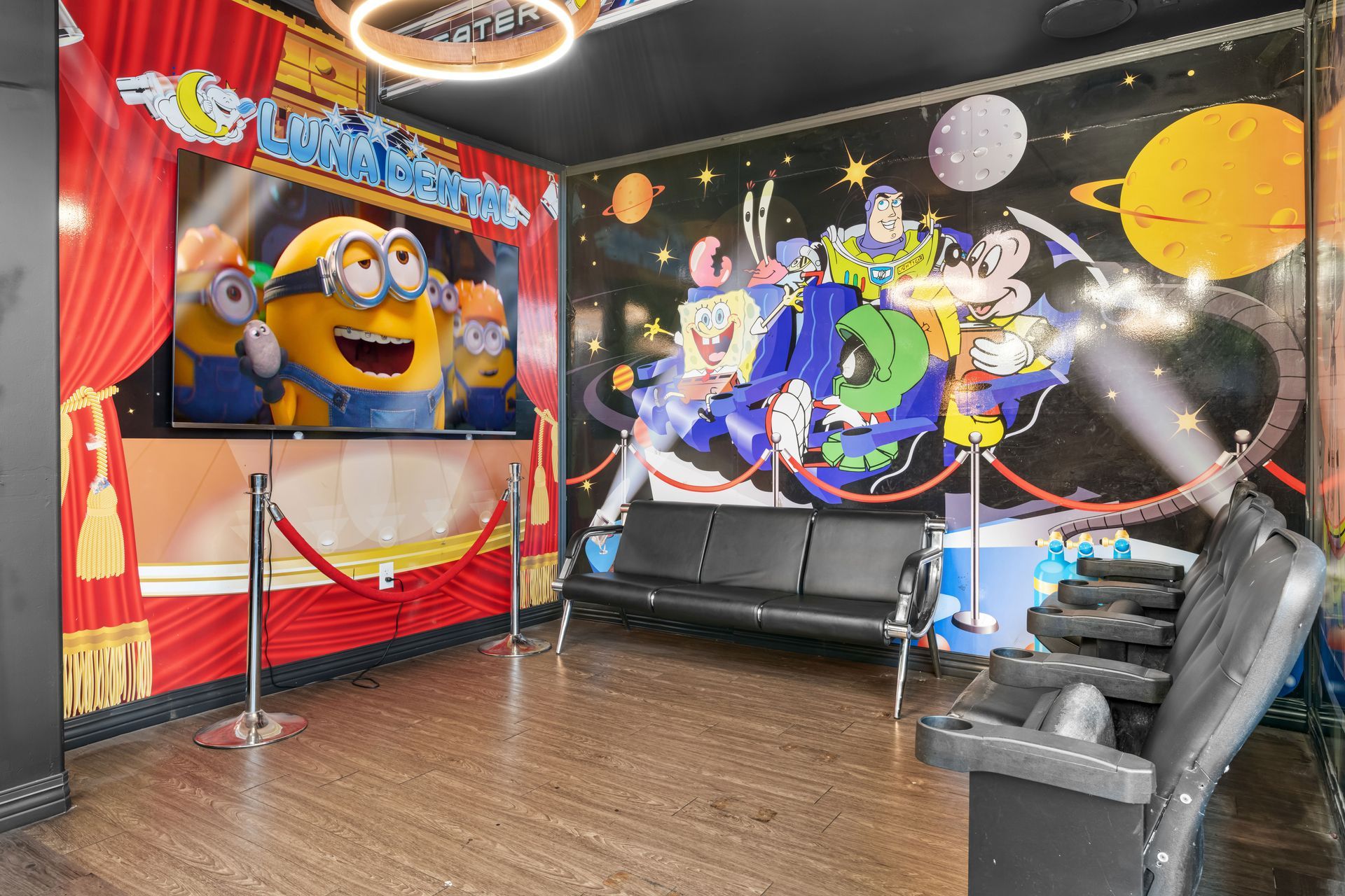 Minions-themed indoor party room with wall murals, black couch, and hardwood floor