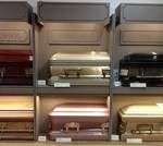 Display of caskets in a funeral home. Various colors and styles on shelves.