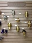 Display of various metal cremation urns on a wall with price tags.