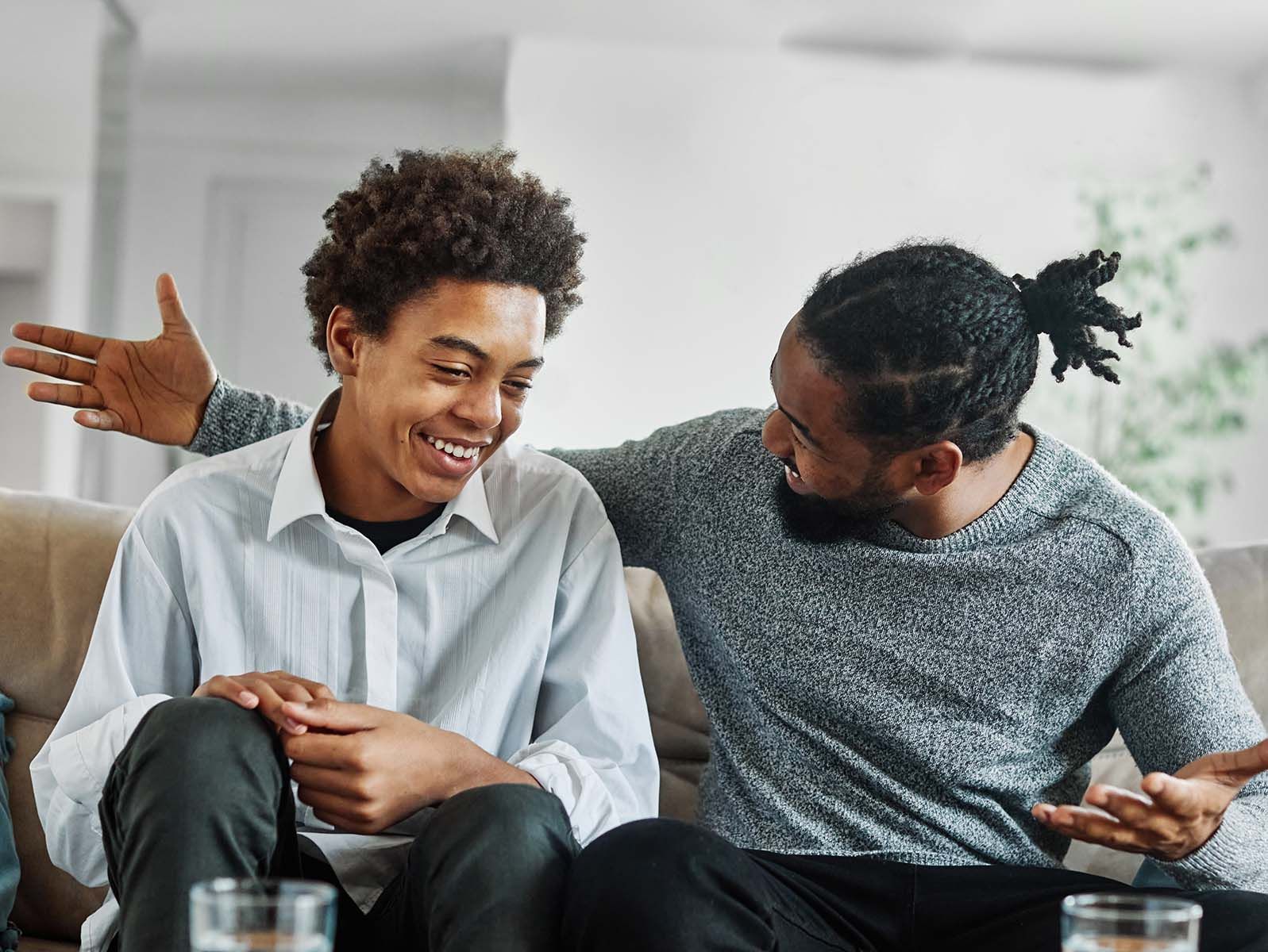Two people sitting on a couch, one with arm around the other, laughing.