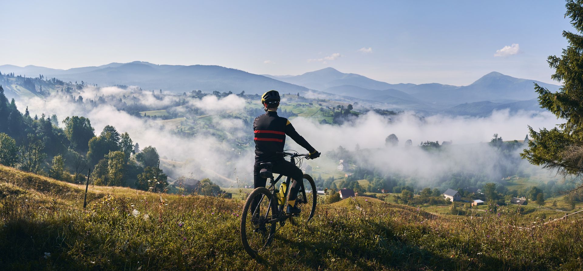 Mountain biker overlooking a misty valley at sunrise, with hills and clouds in the distance