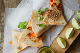 A close up of a quesadilla on a cutting board with limes.