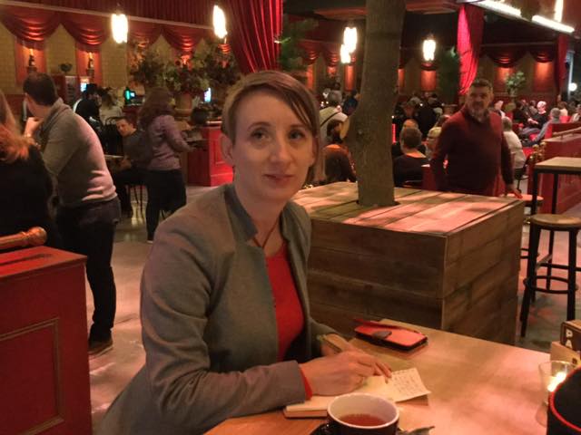 Susanne zit in de foyer van het Studio 100 Pop-Up Theater met een kopje thee en een notitieboekje op tafel.