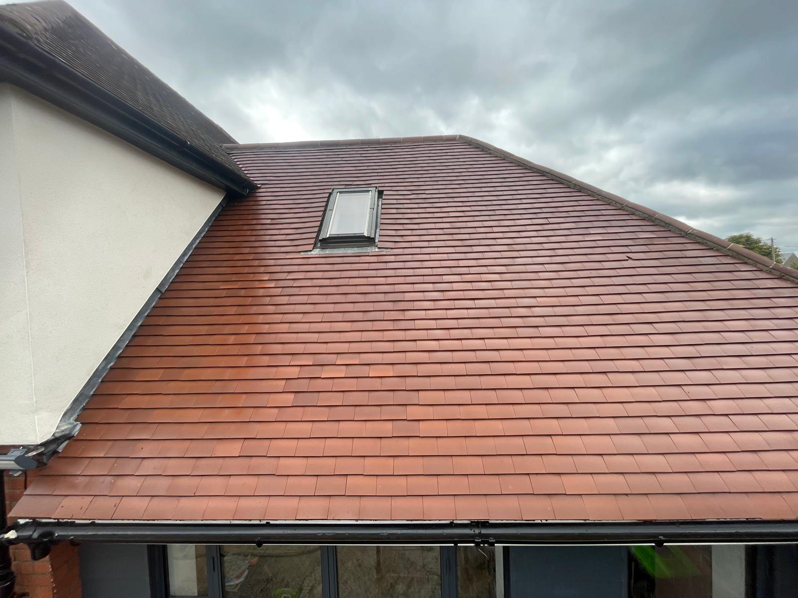 Red tile roof with a skylight, seen from above, on a cloudy day.