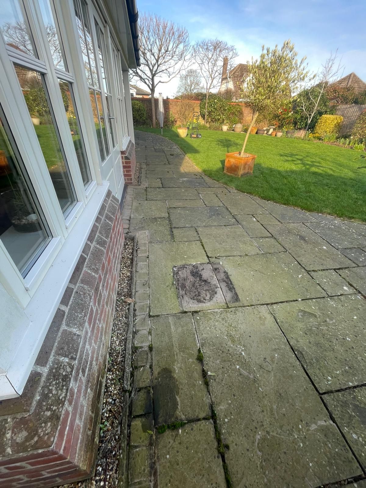 A stone patio walkway lined with gravel runs along the side of a brick house, leading toward a grassy yard with trees.