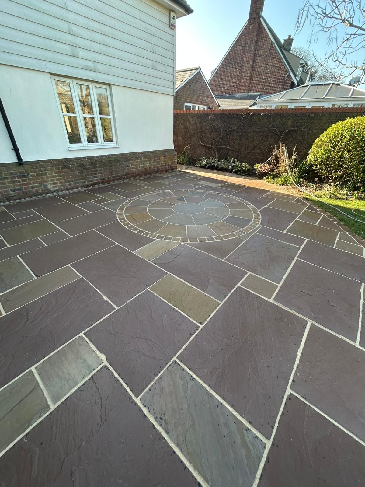 A paved patio made of large, dark-toned rectangular stones featuring a circular stone pattern in the center.