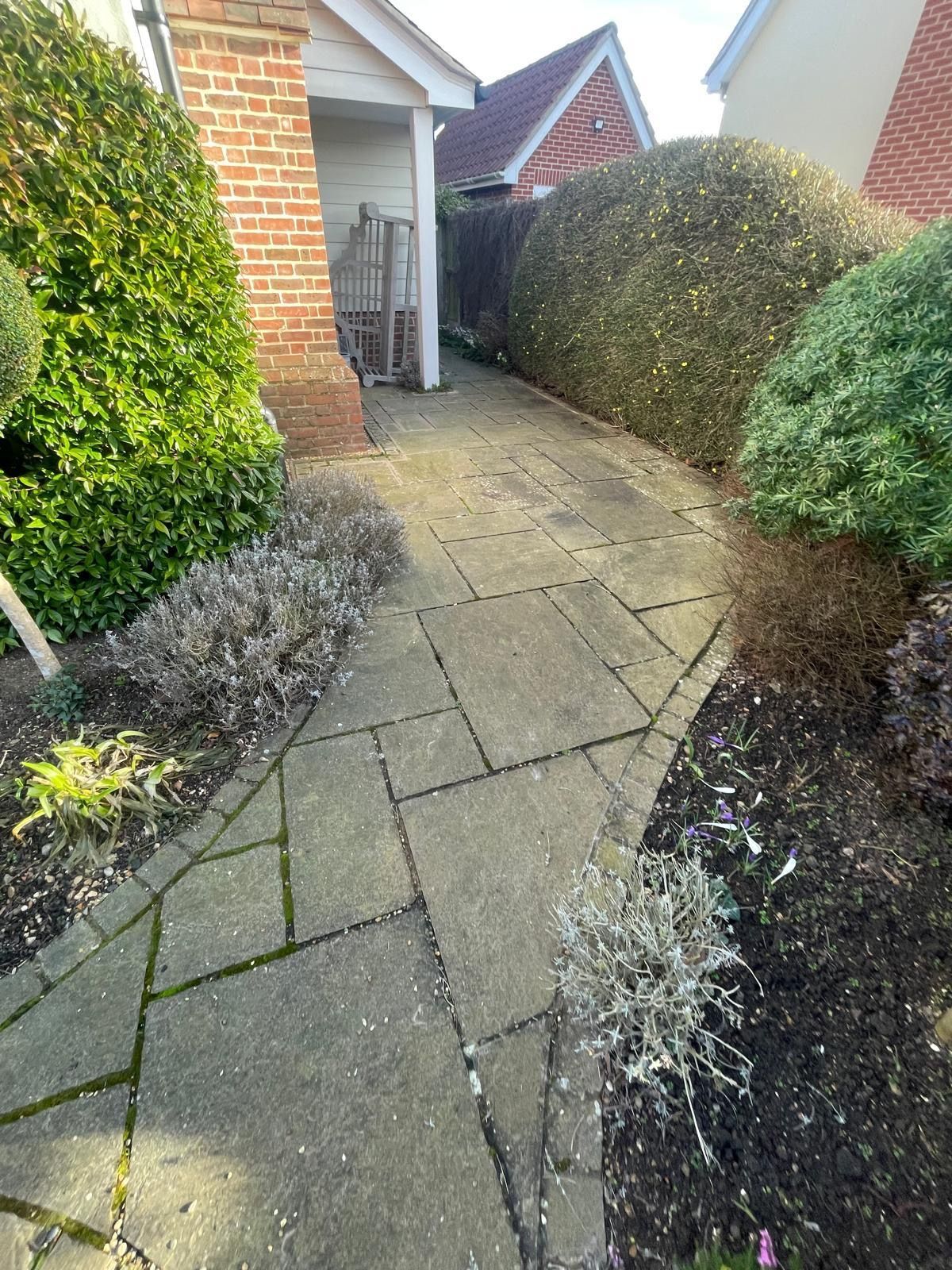 A stone paved garden path leading past large, manicured hedges toward a brick house entrance.