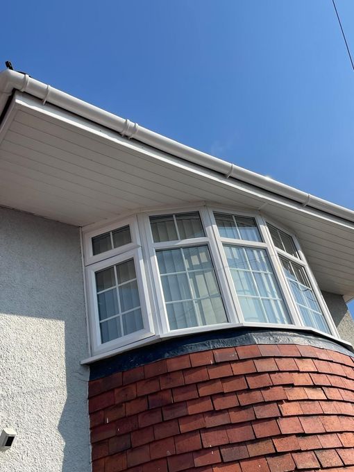 Bay window with white trim, red brick base, under white roof trim, against a blue sky.