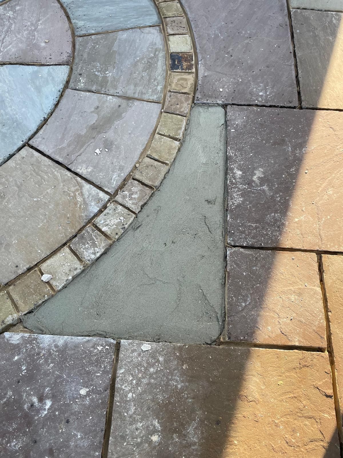 A close-up of a stone patio showing a smooth, grey concrete infill piece adjacent to patterned circular paving stones.