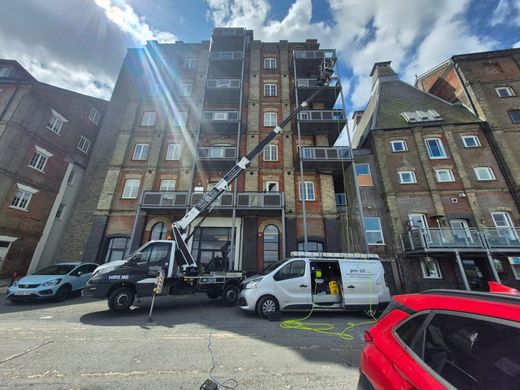 A crane lifting equipment near an apartment building with workers, cars, and a sunny sky.