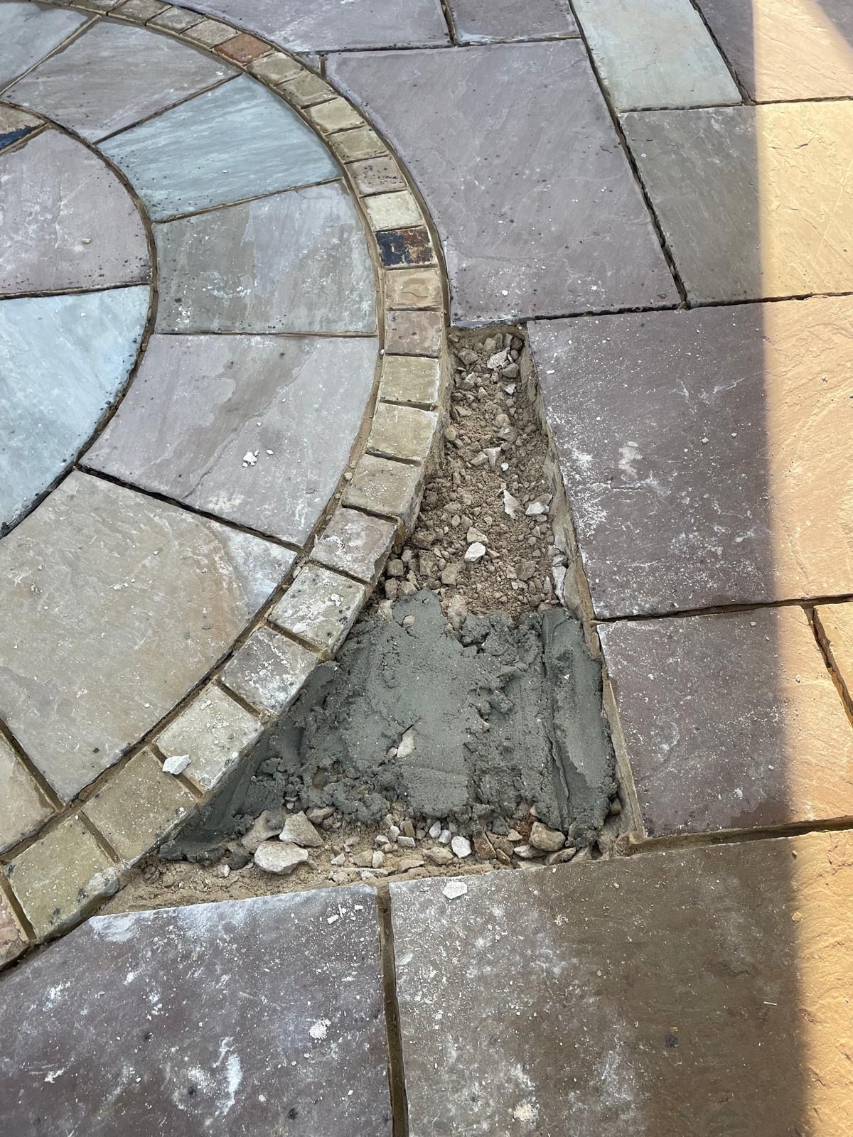 A missing stone paver in a patio, revealing a patch of gray mortar and aggregate against the surrounding stone circle.