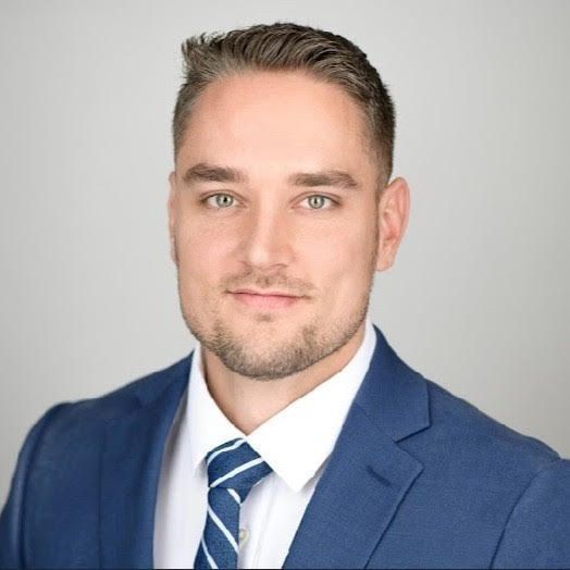 Studio headshot of a man in a blue suit and striped tie on a light background