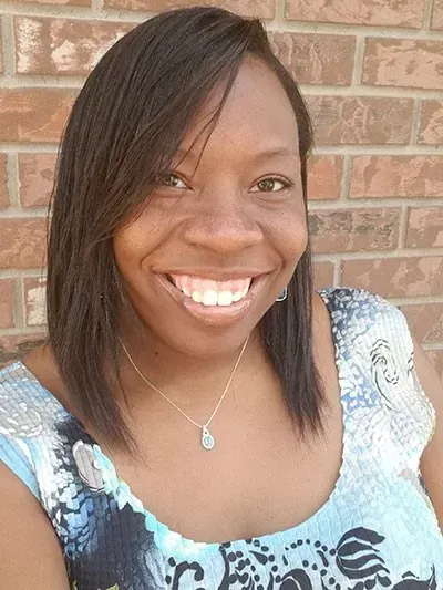 Smiling woman in a light blue patterned top standing in front of a brick wall