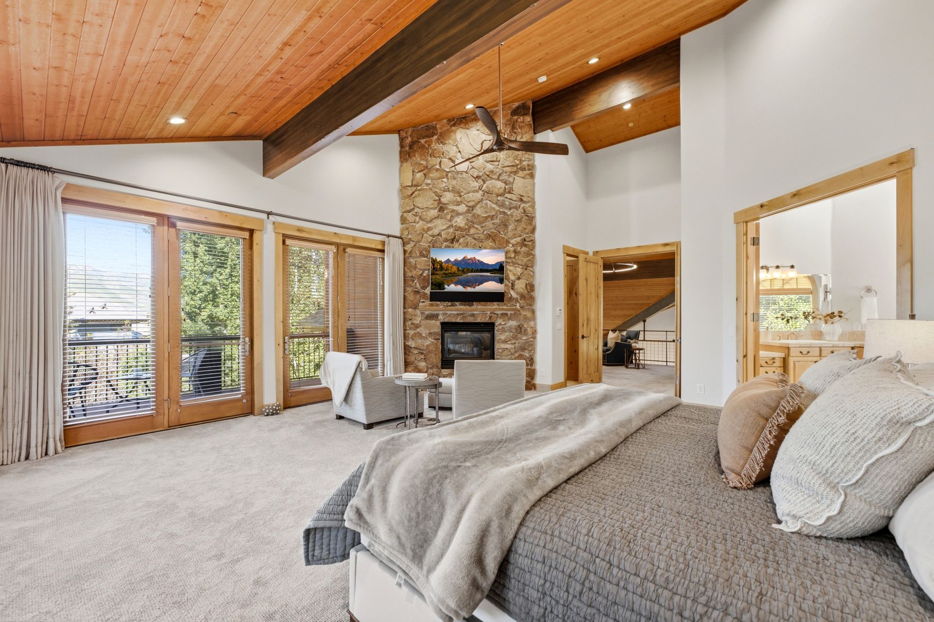 Primary suite at 2490 Silver Cloud Dr with stone fireplace, French doors to the deck, and ensuite bath