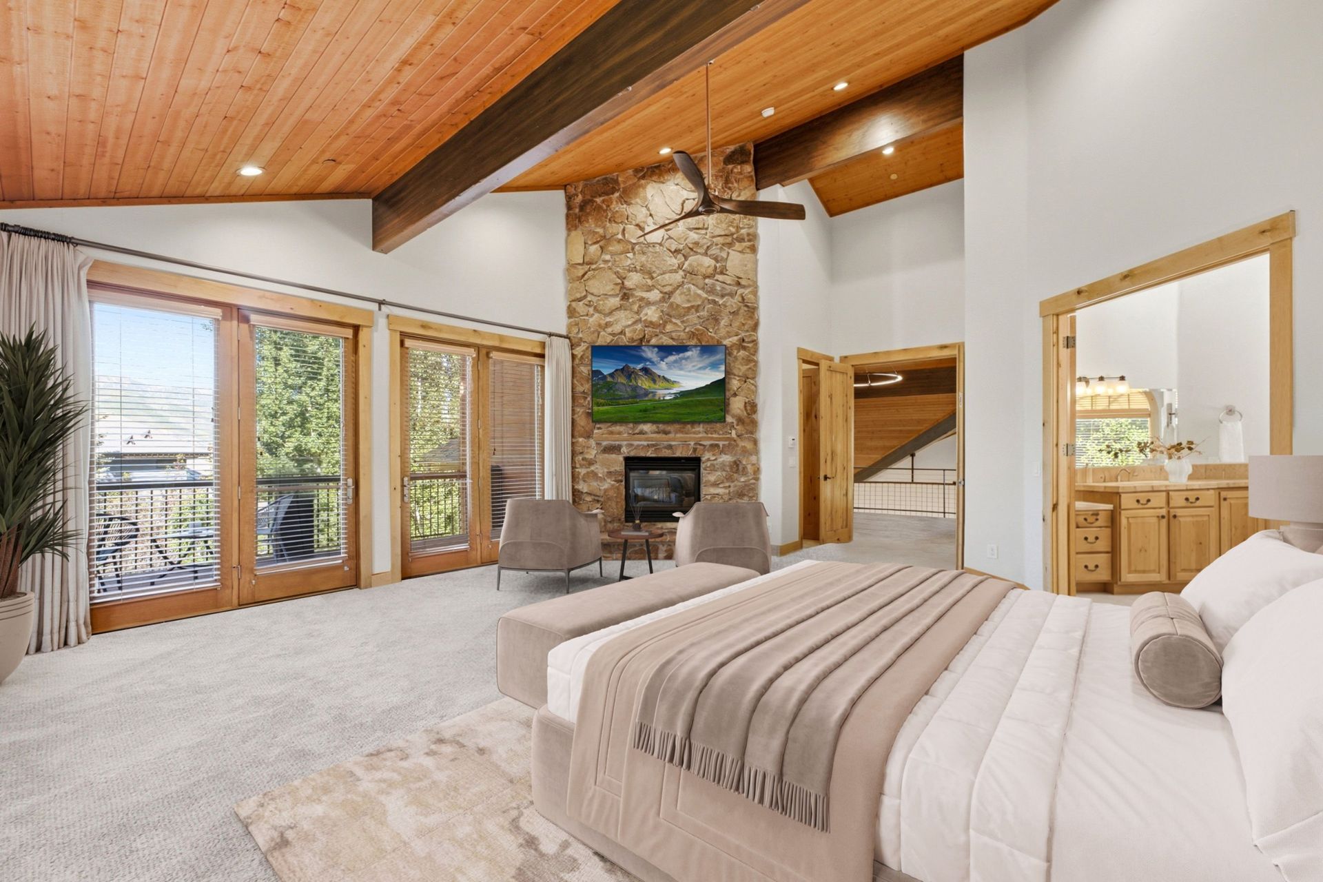 Virtually staged primary suite at 2490 Silver Cloud Dr with stone fireplace, upholstered bed, and French doors to the deck