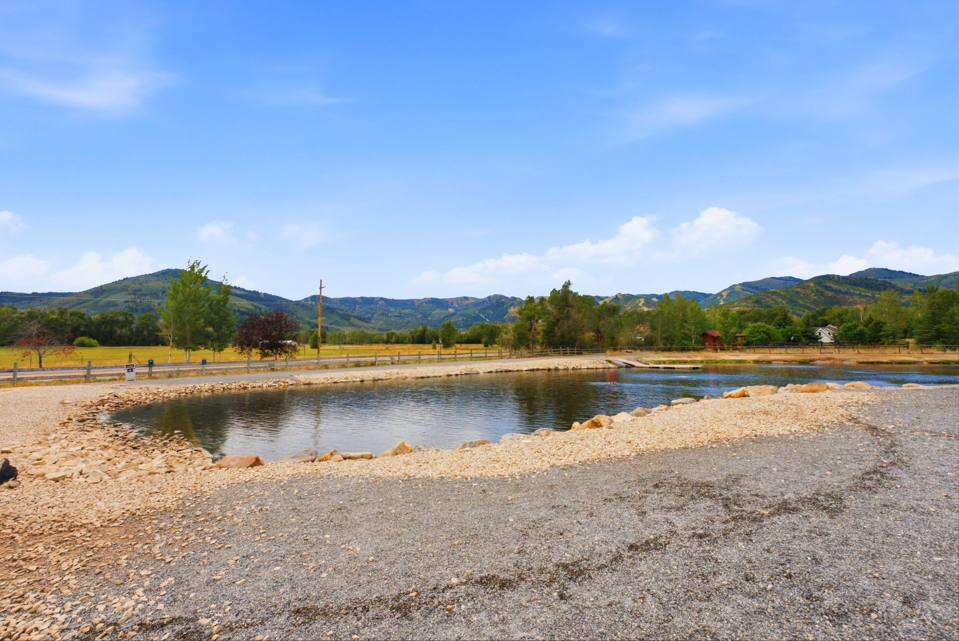 Small pond in a gravel field with trees, hills, and a blue sky in the background