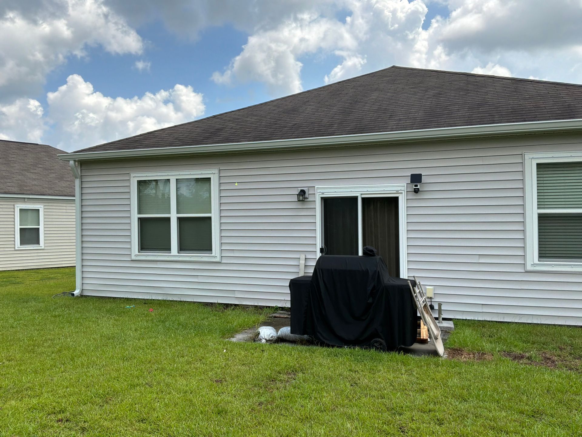 A Charleston Roofs and Windows crew installing a new Atlas architectural shingle roof on a one-story 1960s brick ranch home in West Ashley, SC, with a large live oak shading the side yard and fresh seamless gutters along the eaves, while a W2 project manager checks the ridge line. The photo represents the roofing company serving West Ashley for roof inspections, roof repairs, roof replacements, siding, windows and gutters, rated 4.9 stars across 680 Google reviews.
