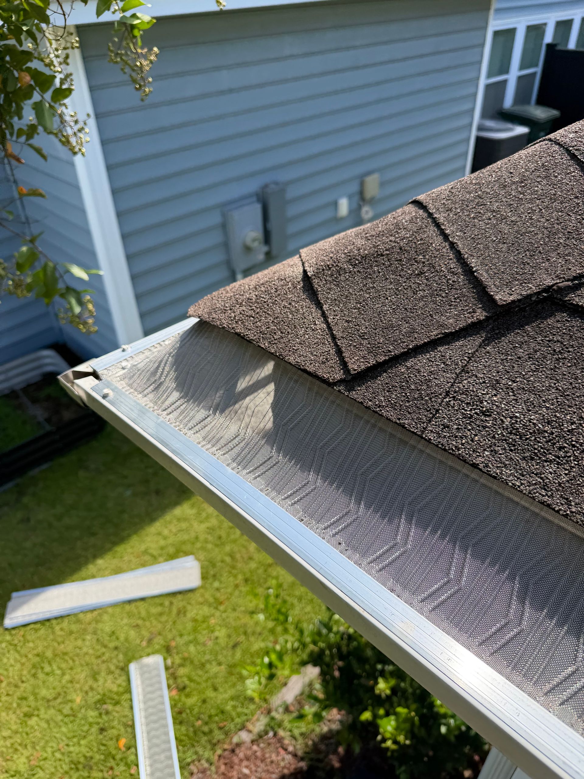 Damaged shingle roof edge with exposed underlayment and detached gutter piece below