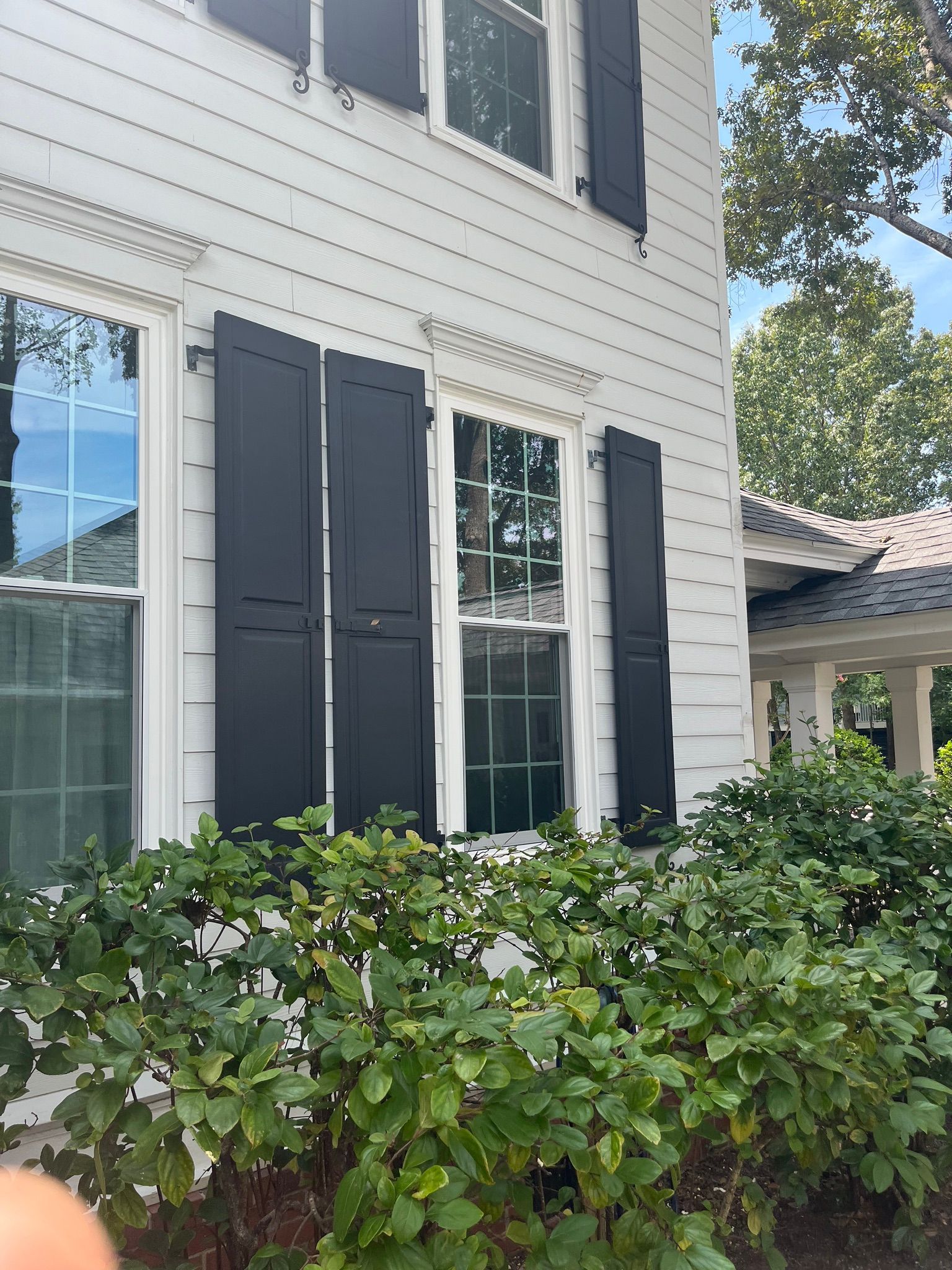 A Charleston Roofs and Windows inspection manager reviewing a line-item roof replacement estimate with a Summerville, SC homeowner on the front porch of a two-story home in a master-planned neighborhood, with the HOA-approved shingle color sample in hand. The image represents roof replacement cost in Summerville SC, priced per square for asphalt shingles, metal and flat roofs, with free inspections and 0% financing for 12 months on approved credit.
