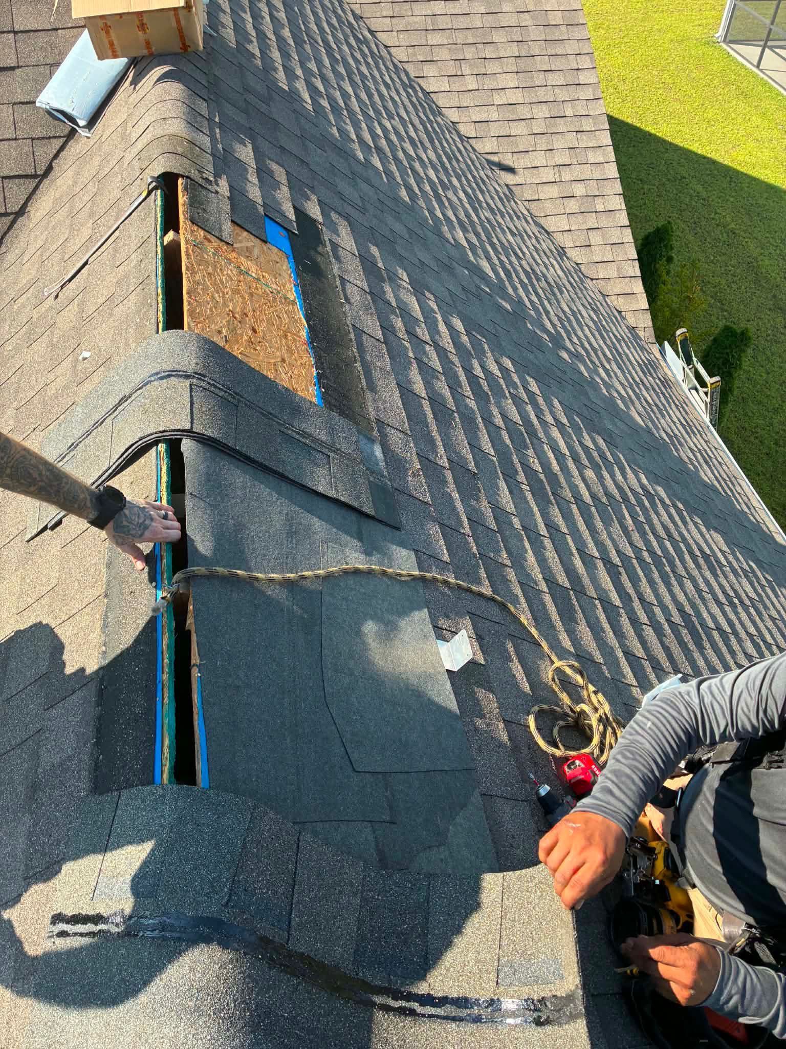 A Charleston Roofs and Windows inspection manager on a ladder photographing a lifted metal roof panel and a worn rubber washer on a Ravenel, SC farmhouse, with pastureland and a line of pine trees behind the home. The image represents the free roof inspection that starts every project in Ravenel, covering everyday leak repairs, emergency roof repairs, full roof replacements and storm damage from wind, hail and tropical storms, backed by a locally owned company founded in 2012.