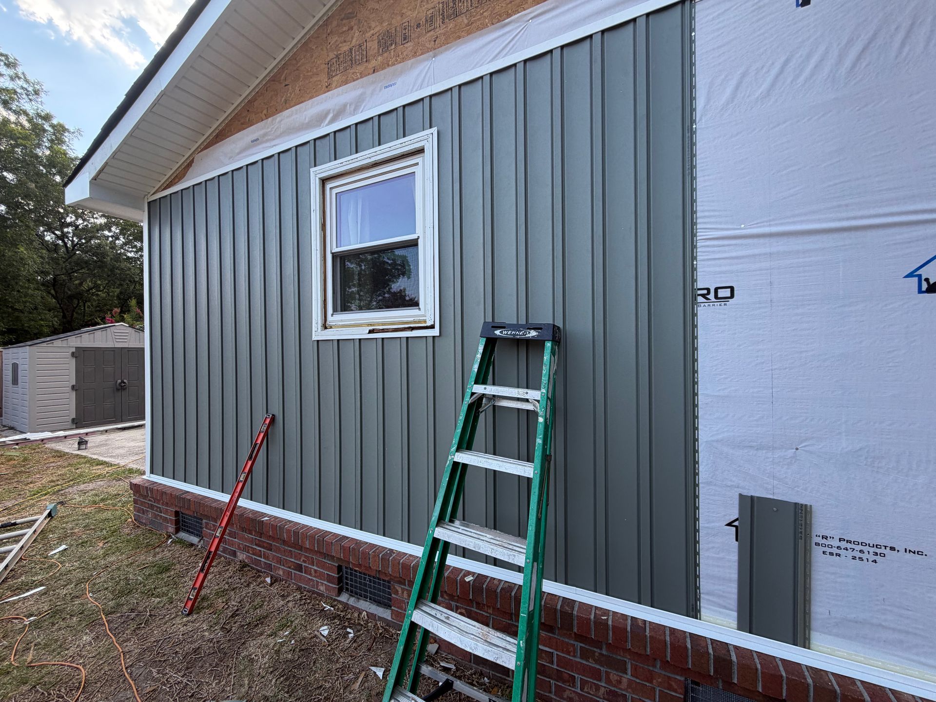 Exterior wall of a house with gray siding, a small window, and a green ladder leaning below it