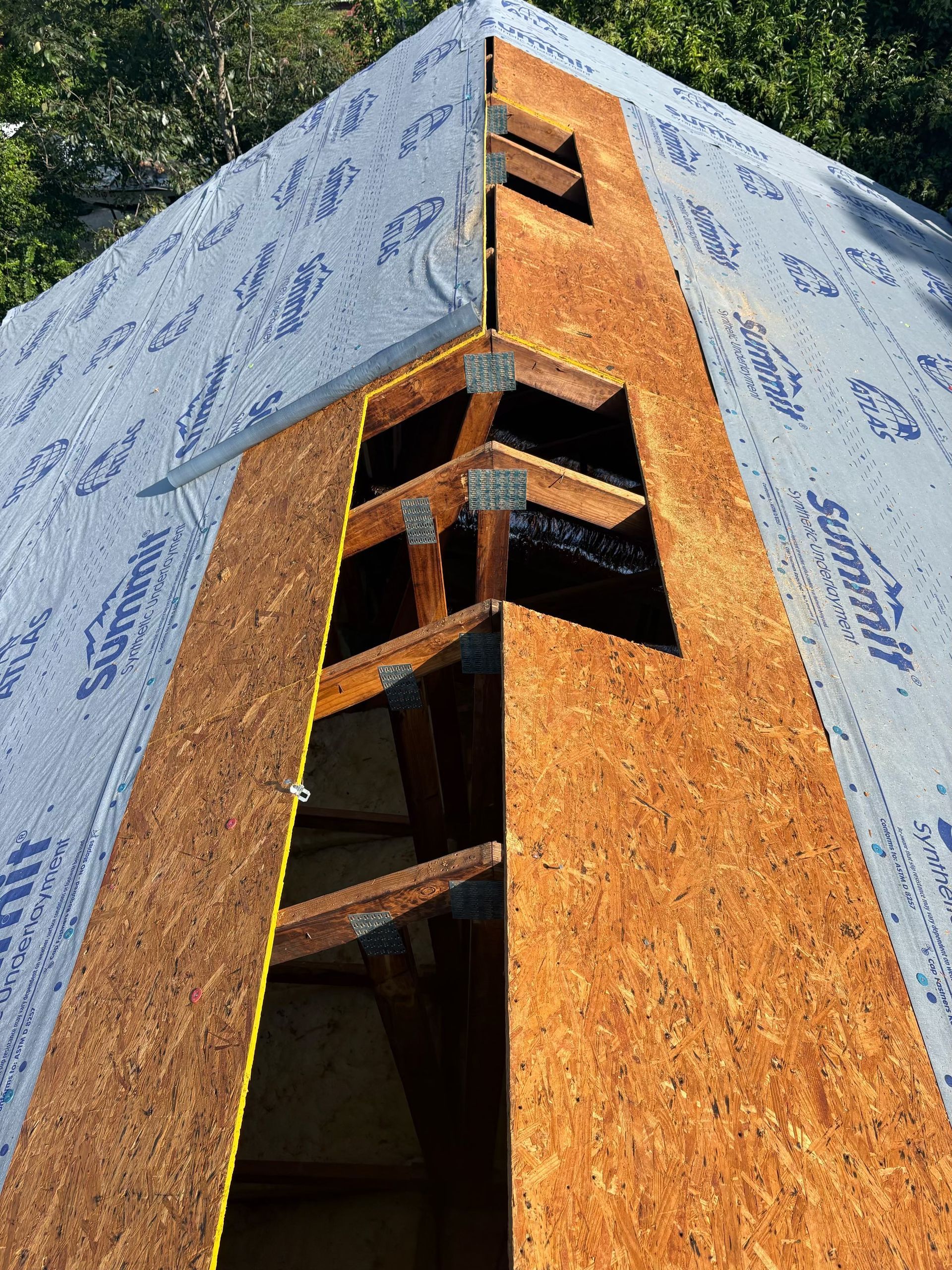 Wood-frame building under construction with OSB siding and blue house wrap on the upper walls