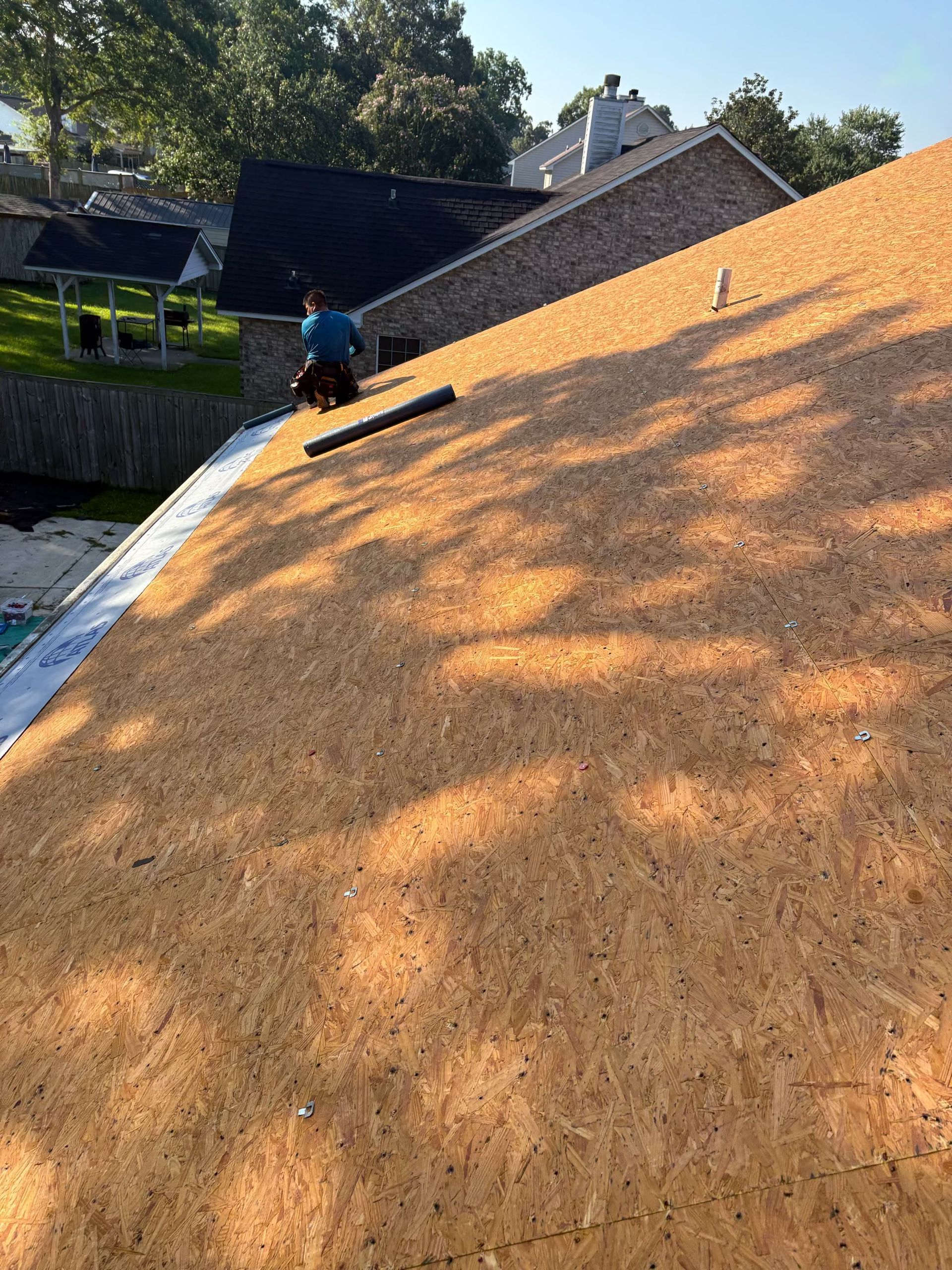 A Charleston Roofs and Windows inspection manager on a ladder photographing lifted shingles and a cracked pipe boot on a two-story vinyl-sided home in a Ladson, SC subdivision near I-26, while the homeowner watches from the driveway. The image represents the free roof inspection that starts every Ladson project, from small roof repairs and emergency leak calls to full roof replacements and storm damage repair after wind and hail.