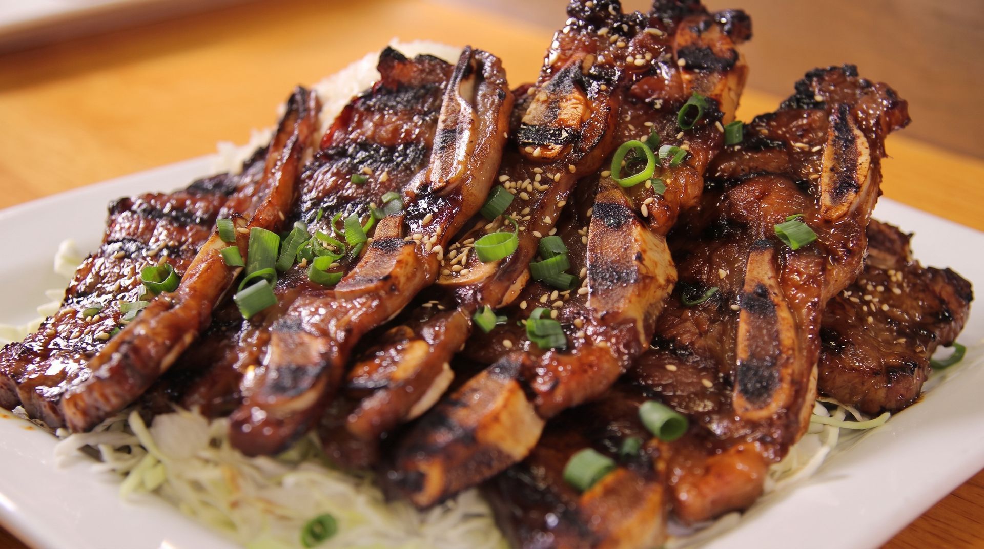 Grilled steak slices glazed with sauce, garnished with green onions on a white plate.