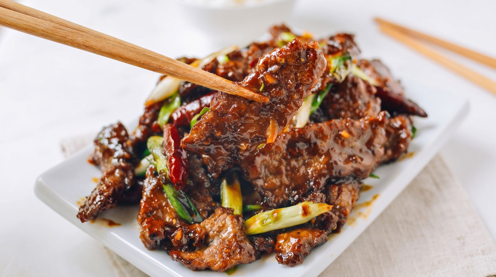 Chopsticks lifting spicy grilled meat and vegetables on a white plate