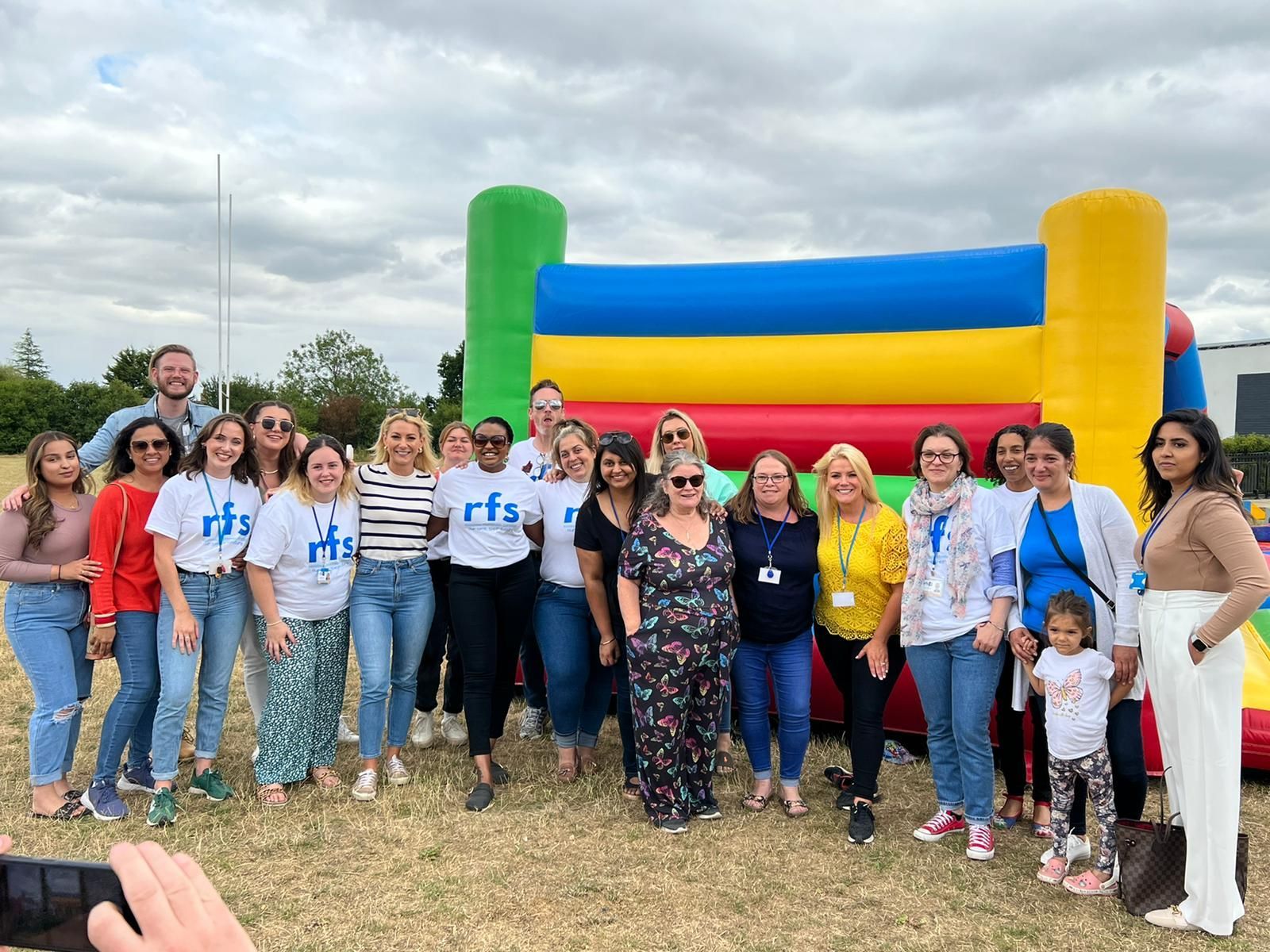 Group of people smiling, posing in front of a colorful bouncy castle. Outdoor event.