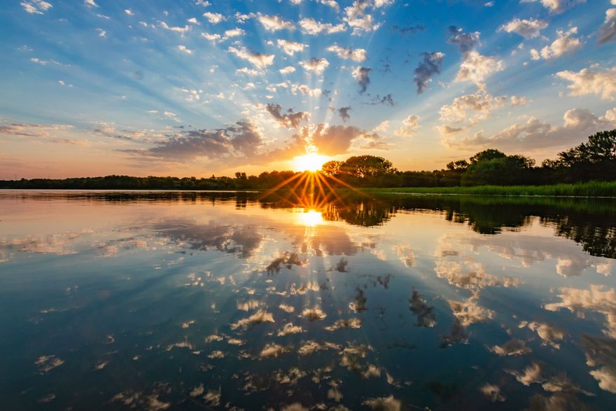 Sunset over a calm lake, with golden light reflecting in the water and clouds overhead.