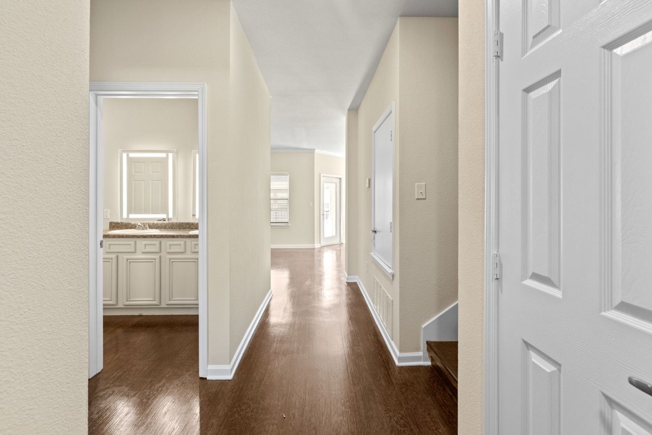 Interior apartment hallway with doors, wooden floor, and a visible bathroom vanity.