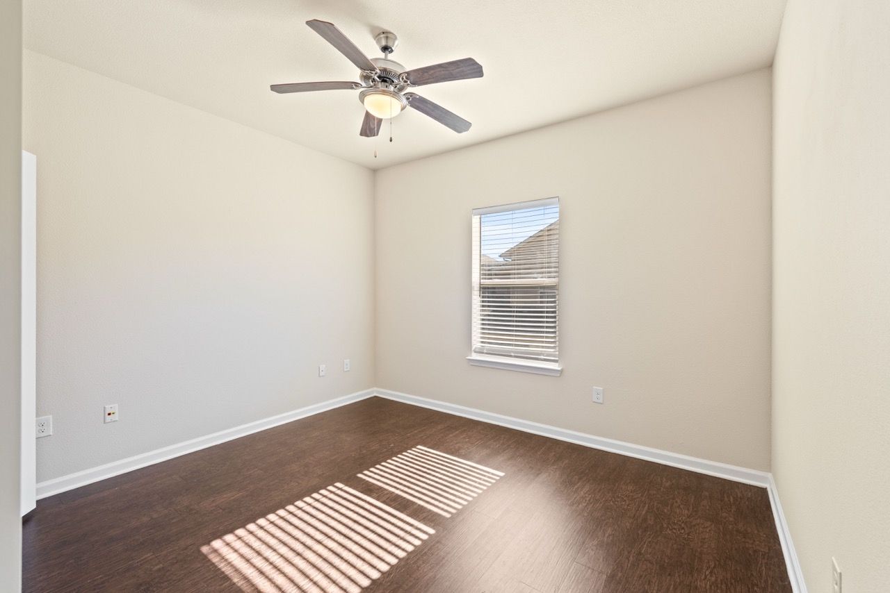 Empty bedroom with dark wood floor, window with blinds, and a ceiling fan.