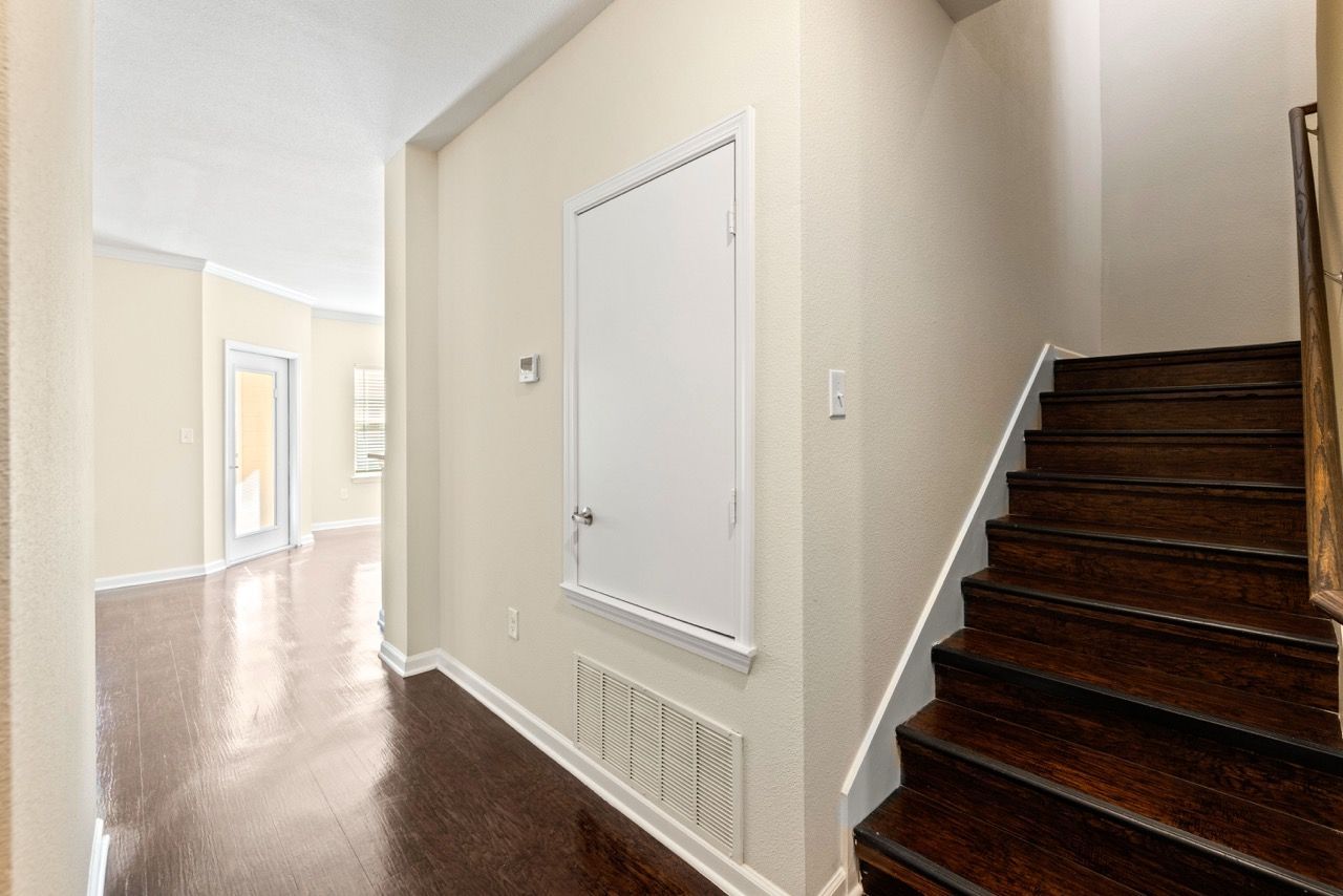 Hallway inside an apartment with beige walls, dark wood stairs, and a white utility panel.