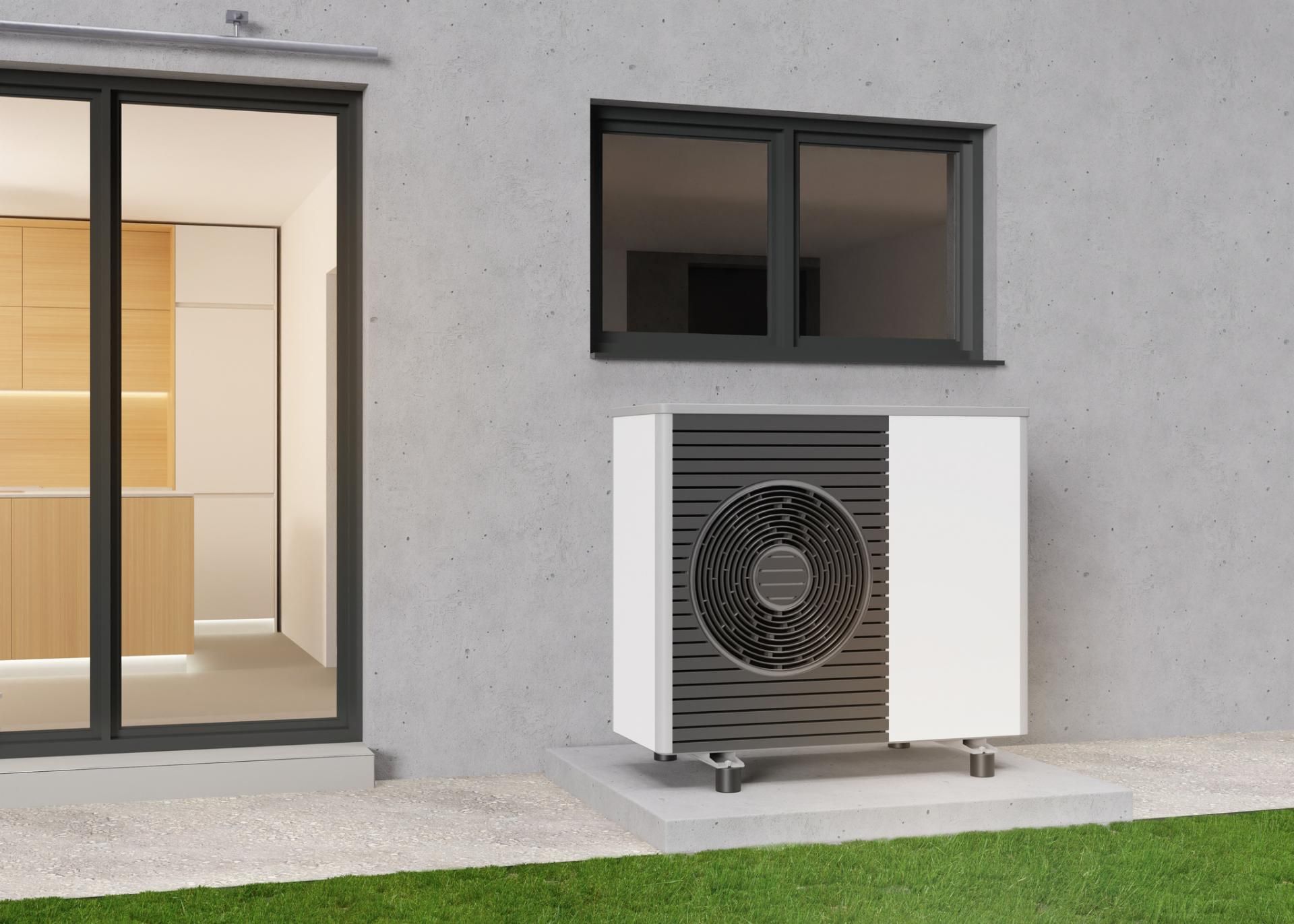 Unità di pompa di calore all'esterno di una casa, accanto a una finestra e una porta, montata su una lastra di cemento.