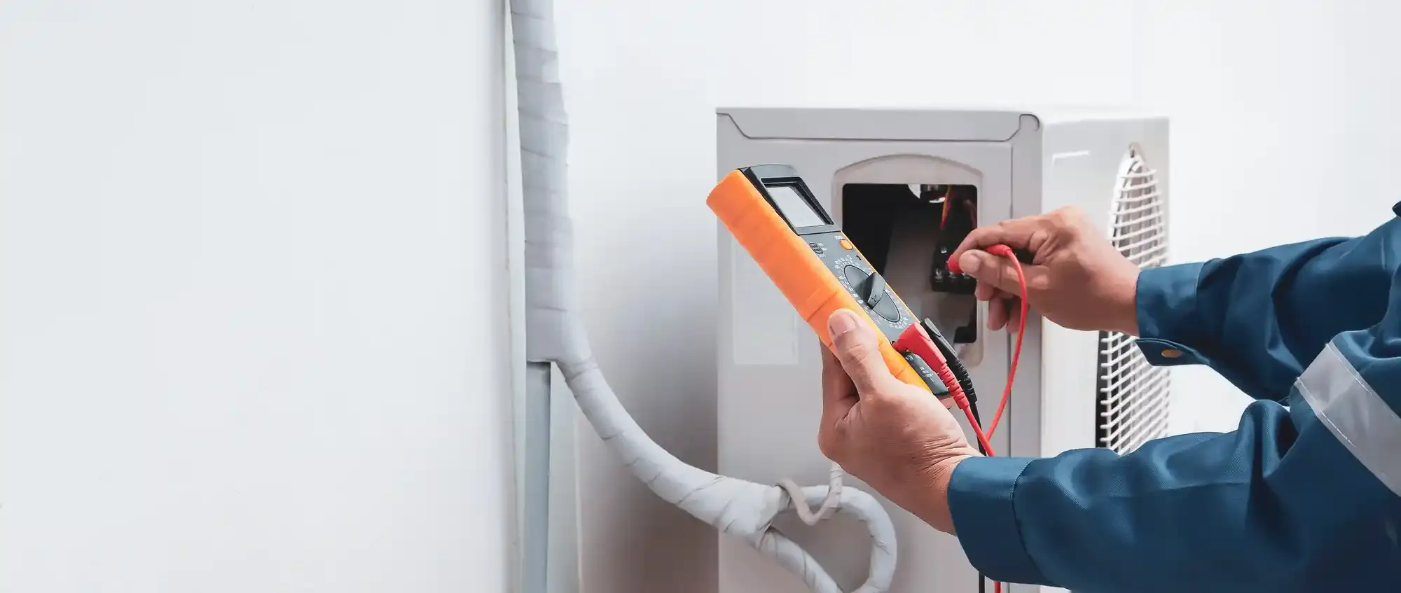 Un elettricista utilizza un multimetro per controllare i fili all'interno di un elettrodomestico bianco.