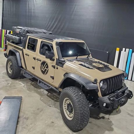 Tan off-road Jeep with black accents and rugged tires parked indoors on a concrete floor.