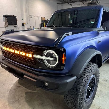Blue off-road SUV with a black hood and amber grille lights in a garage