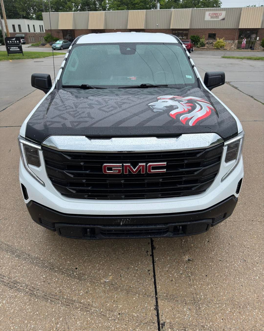 Front view of a black and white GMC pickup with a red claw graphic on the hood, parked on a wet lot