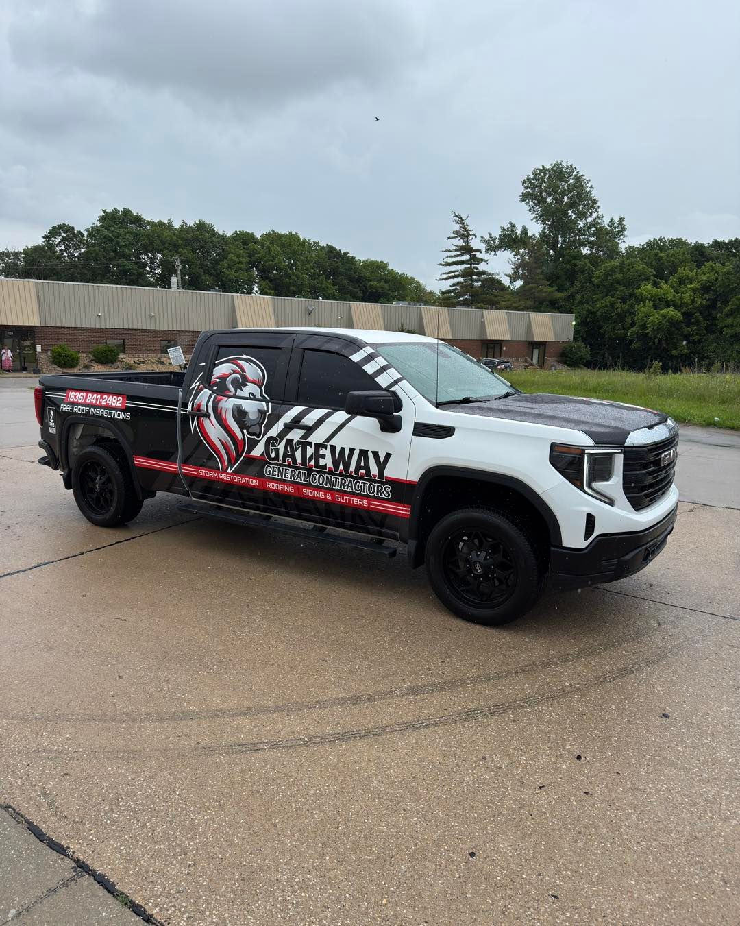 White and black pickup truck with graphic logo parked on wet pavement near trees