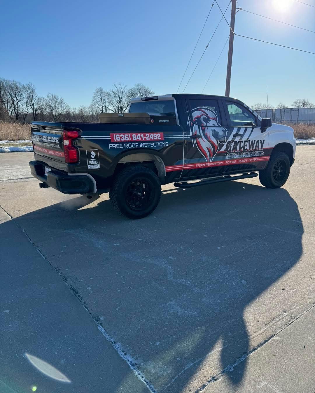 Black custom pickup truck parked on a sunny road, with red and white graphics on the side.