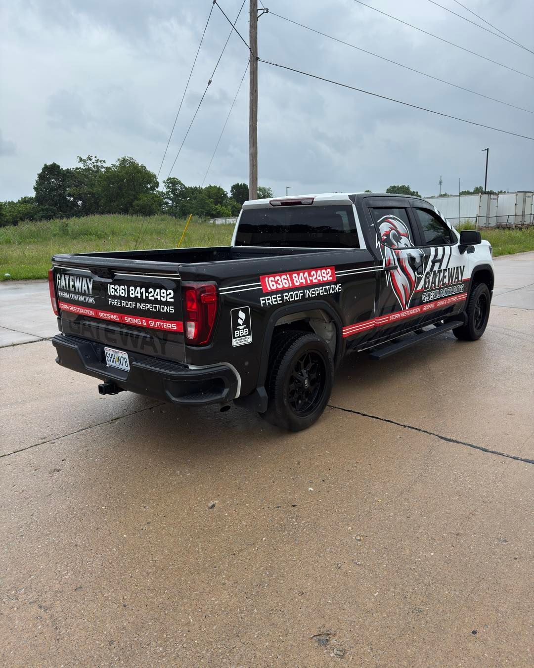 Black pickup truck with racing decals parked on a wet road under cloudy skies.