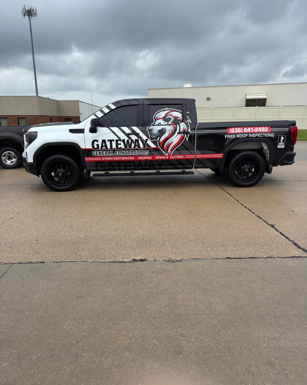 Black pickup truck with large red-and-white graphic parked on a wet roadside under cloudy skies