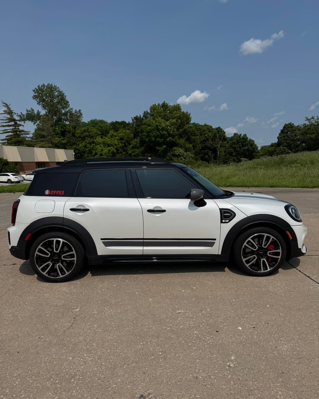 White Mini Cooper parked on asphalt under a blue sky, side view with black roof and red accents